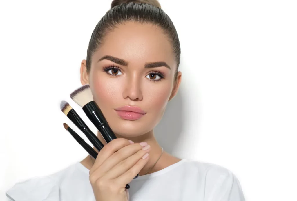 Młoda kobieta z makijażem no make-up look trzyma pędzie