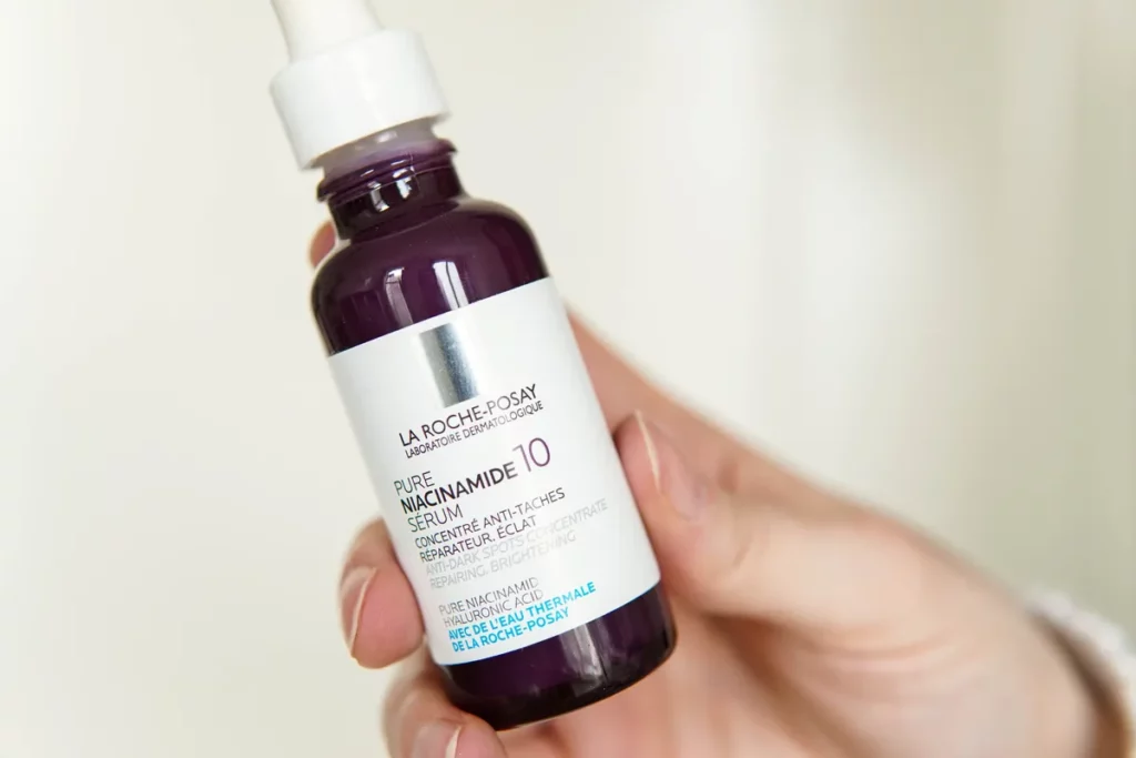 Fioletowa butelka serum La Roche-Posay z pipetą trzymana w dłoni na jasnym tle.