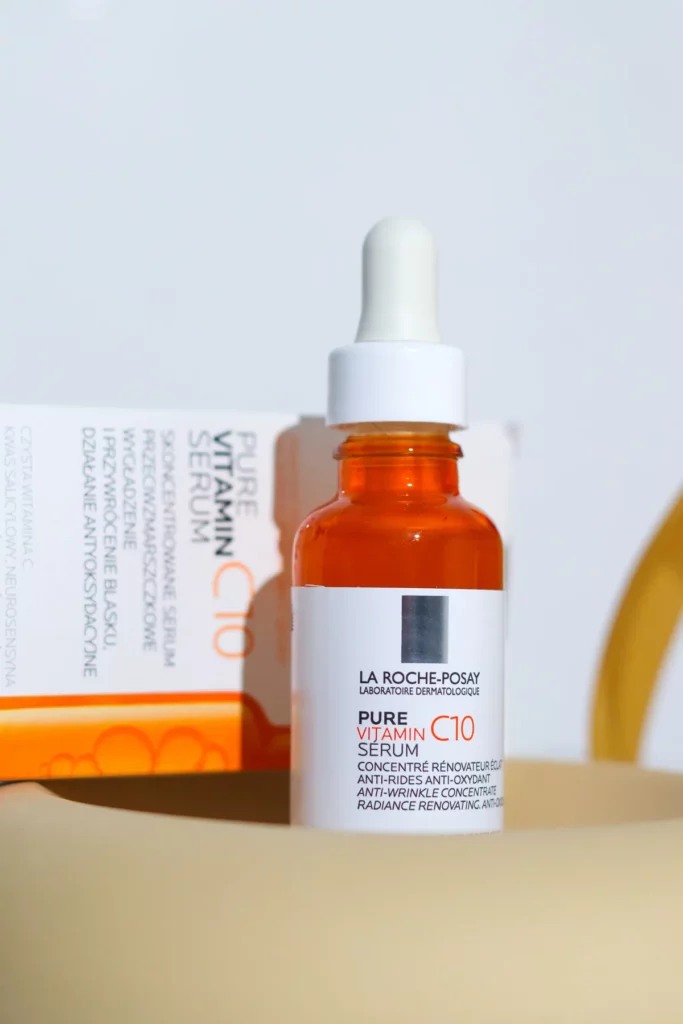 Buteleczka serum z witaminą C stoi z kroplomierzem na jasnym tle obok opakowania.