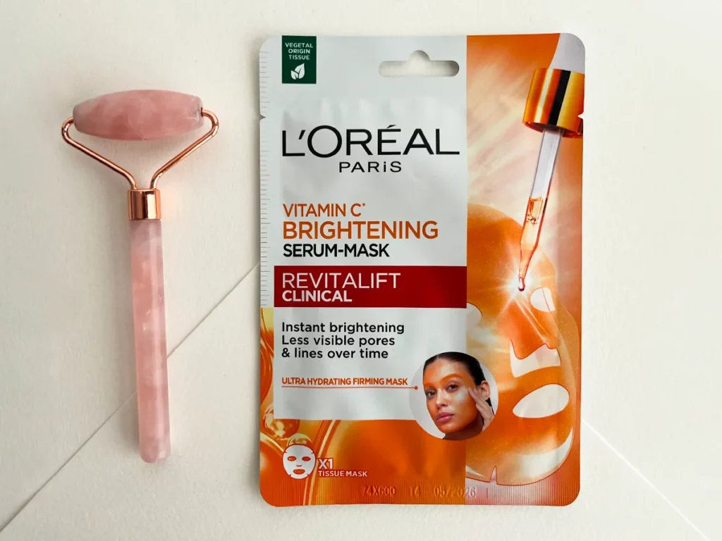 Maseczka L’Oréal Paris Revitalift Clinical Vitamin C z różowym rollerem po lewej stronie na białym tle - zdjęcie.