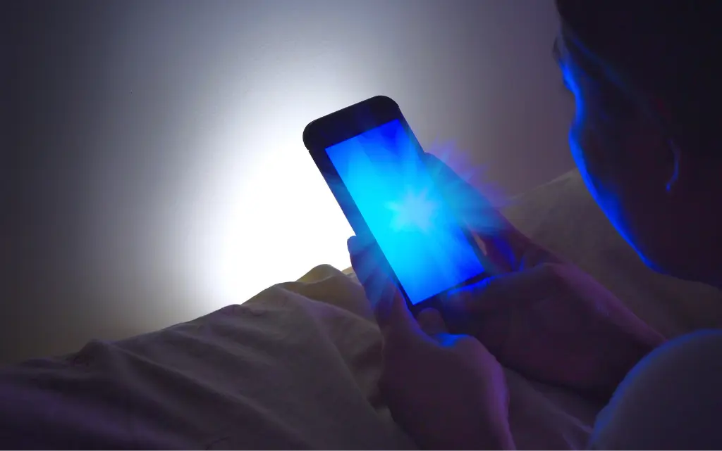 Nastolatka trzyma w ręku smartfon, który emituje niebieskie światło 