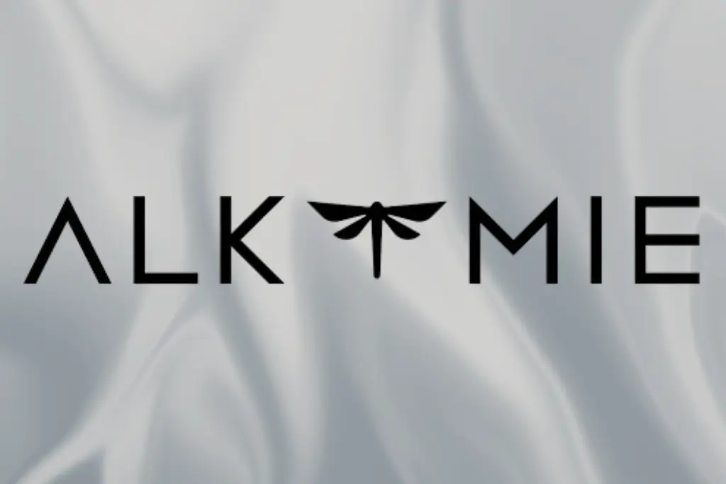 Czarny logotyp "ALKIMIE" z sylwetką ważki pośrodku na jedwabistym, szarym tle.