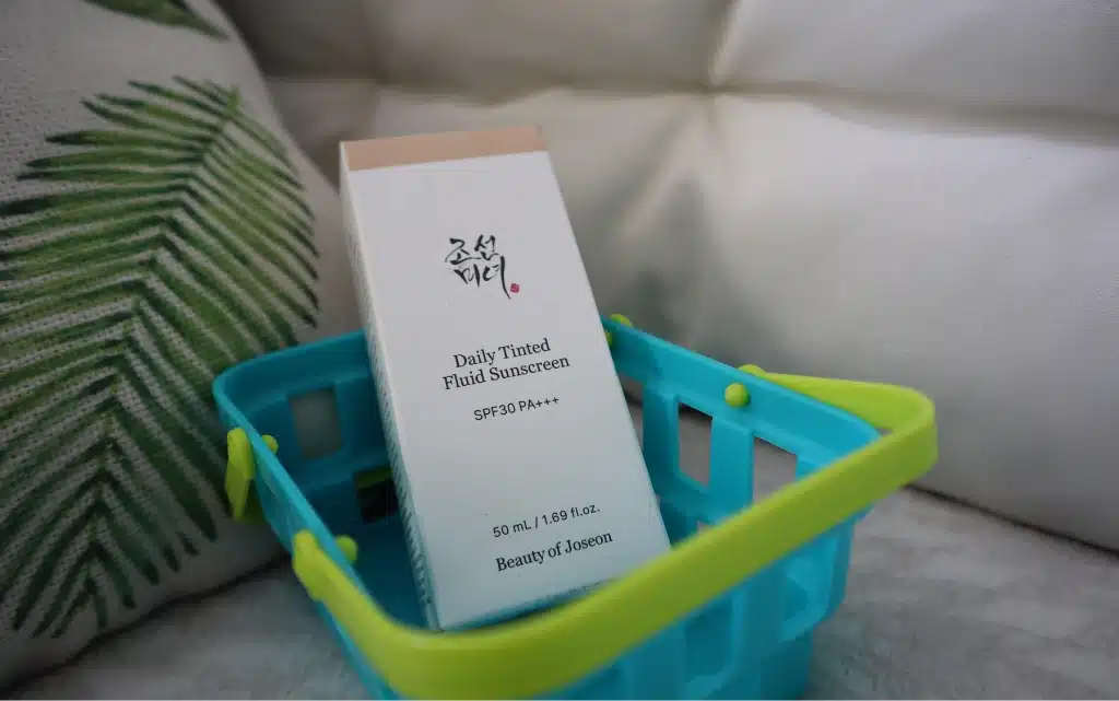 Opakowanie tintu Daily Tinted Fluid Sunscreen Beauty of Joseon w niebieskim koszyczku na tle poduszek 