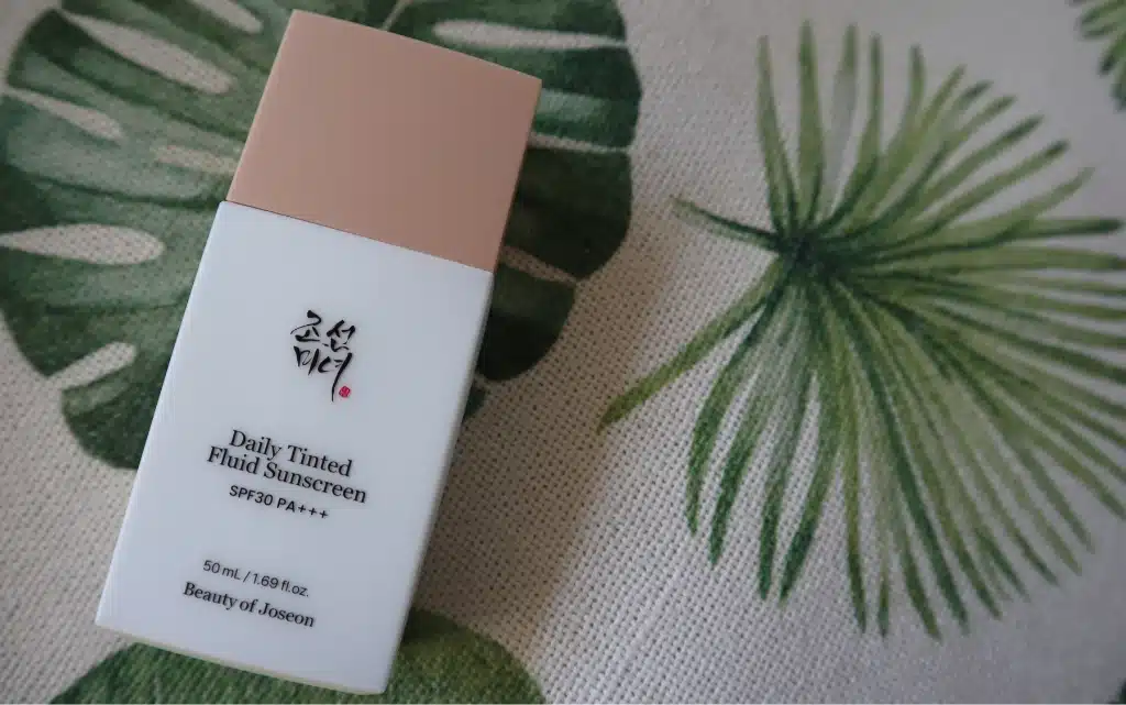 Butelka tintu Daily Tinted Fluid Sunscreen Beauty of Joseon na tle beżowo zielonej poduszki 