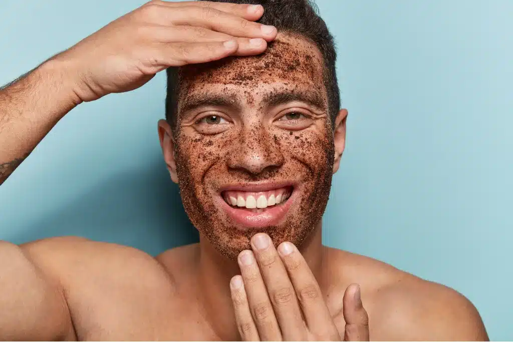 Uśmiechnięty młody mężczyzna wykonuje peeling twarzy