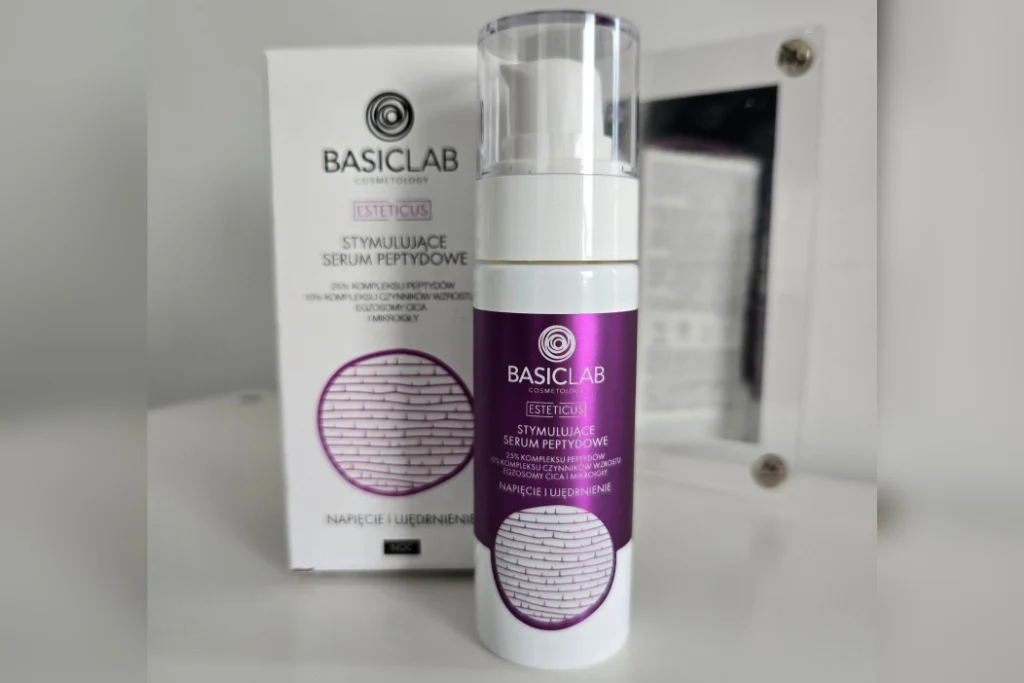 Butelka serum BasicLab z fioletową etykietą stoi przed opakowaniem na białej półce przy lustrze.