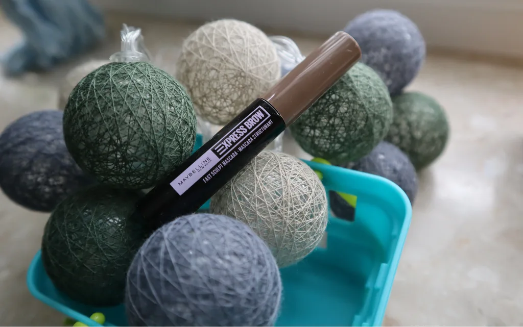 Maskara do brwi Maybelline NY Express brow Sculpt w niebieskim koszyczku i wśród lampek cotton balls