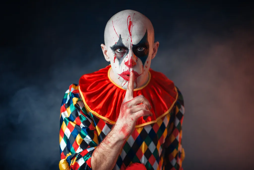 Przebrany za klauna na Halloween mężczyzna pokazuje znak ciszy palcem na ustach