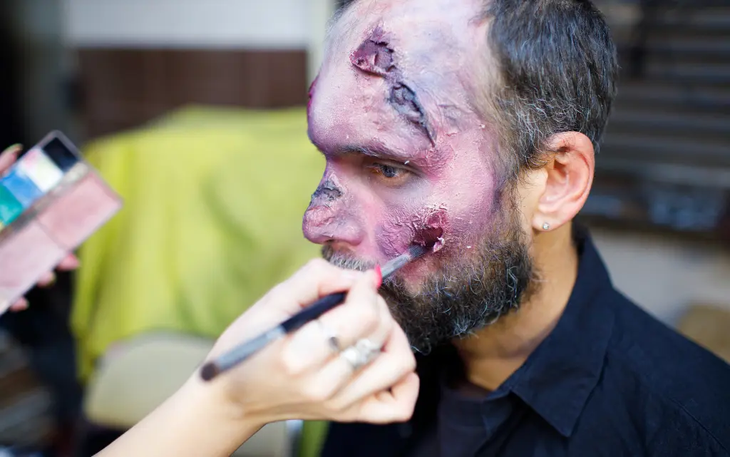 Męzczyzna u wizażystki ma wykonywany makijaż na Halloween z rozdrapanymi ranami twarzy