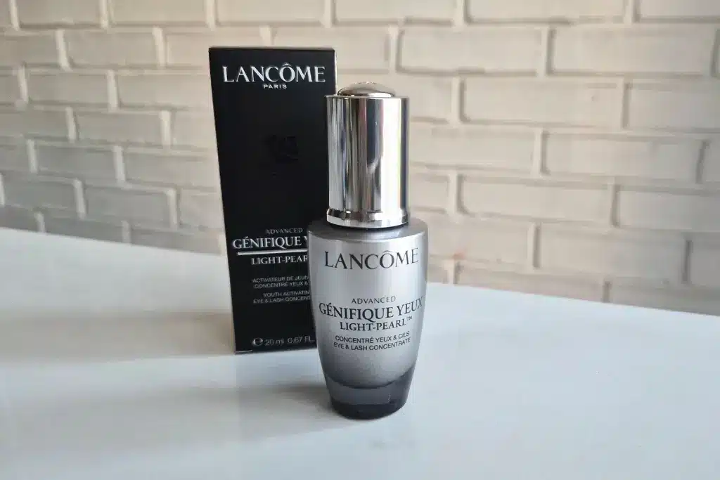 Butelka serum Lancôme stoi przed czarnym pudełkiem na białym blacie, ceglana ściana w tle.