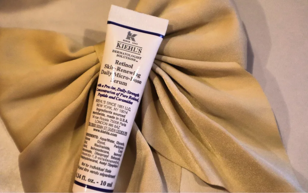 Opakowanie 10 ml serum z retinolem Kiehl’s Retinol Skin-Renewing Daily Micro-Dose Serum  na tle jedwabnej kokardy do włosów 