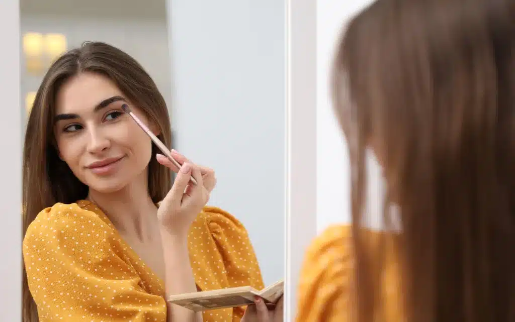  Kobieta maluje oczy cieniami przed lustrem 