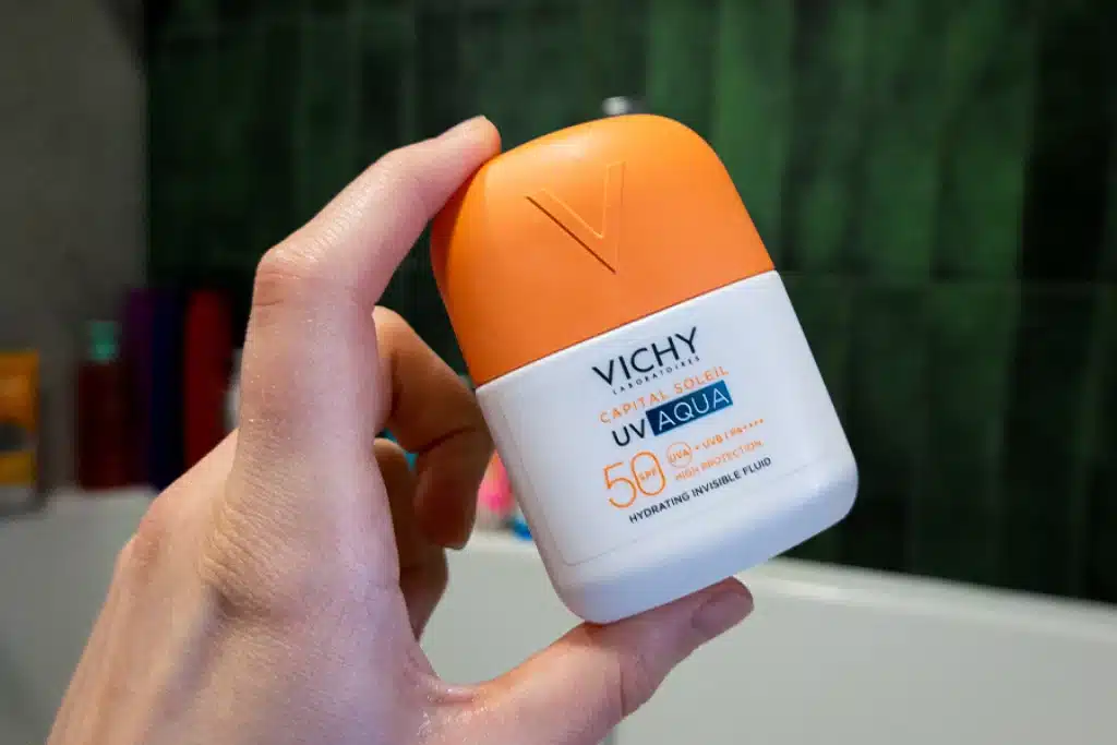 Vichy Capital Soleil UV-Aqua Fluid SPF50 trzymany w kobiecej dłoni, zielone tło