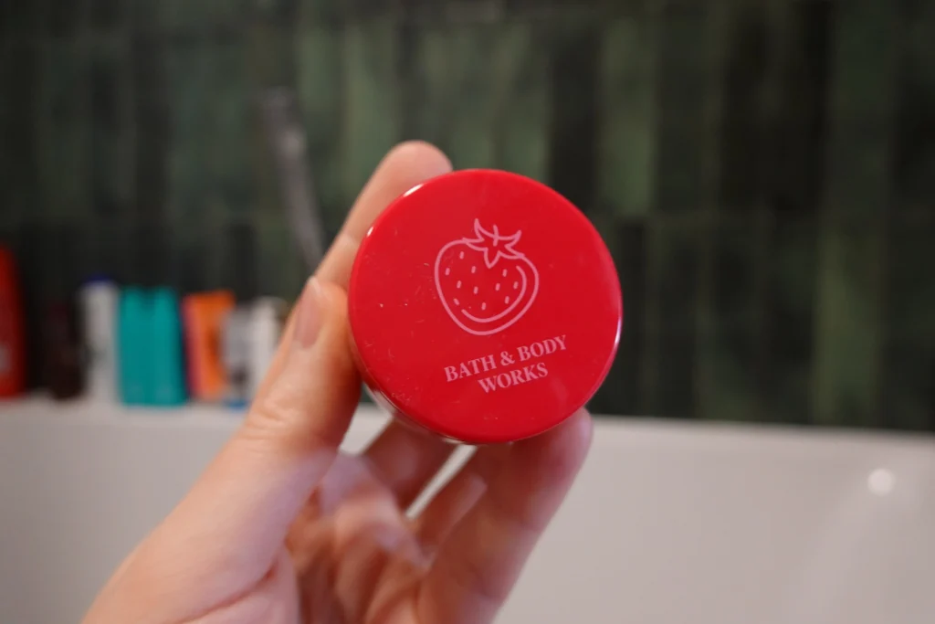 Bath & Body Works Strawberry Pound Cake Peeling do ust trzymany w kobiecej dłoni na tle łazienki